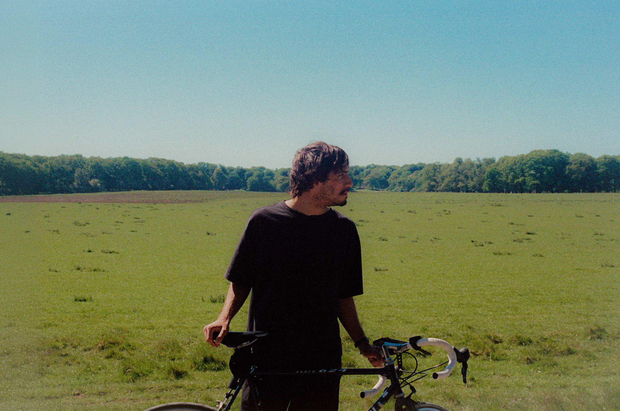 Alê standing with his bicycle in a grassy field